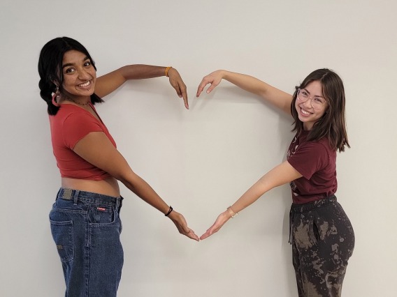 Asia Richardson and Pulari Kartha, creating a heart with their arms, smiling towards the camera