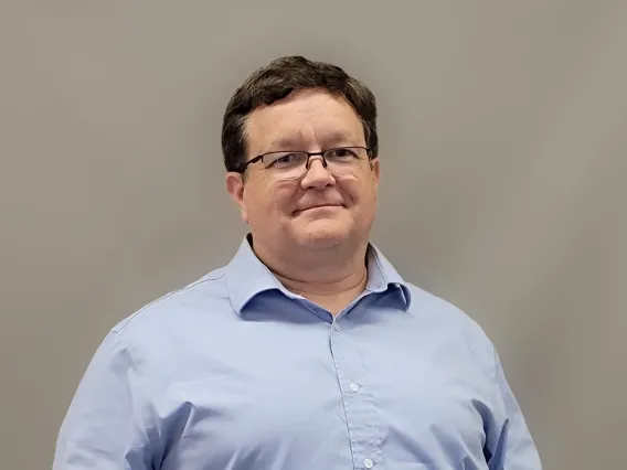 Craig Aspinwall smiling towards the camera wearing a light blue button up collar shirt