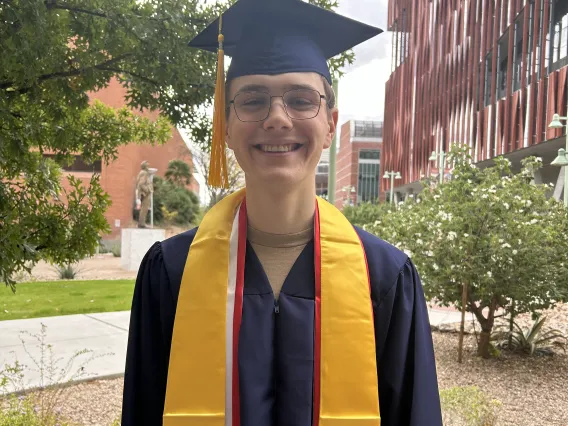 Caleb Seekins stands with large smile in cap and gown