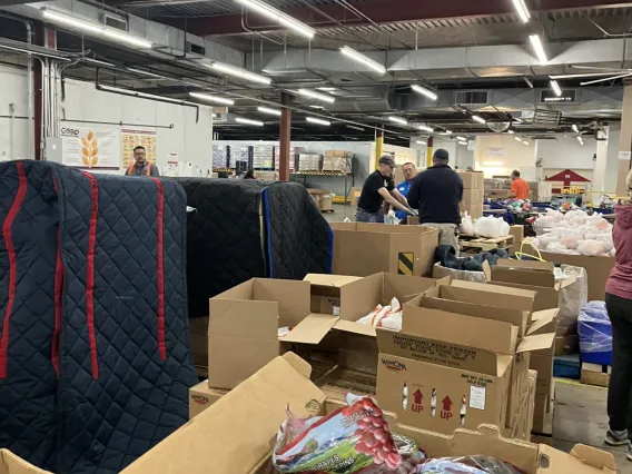 Workers stand in the background with pallets full of items to be distributed to those in need at the Community Food Bank of Southern Arizona