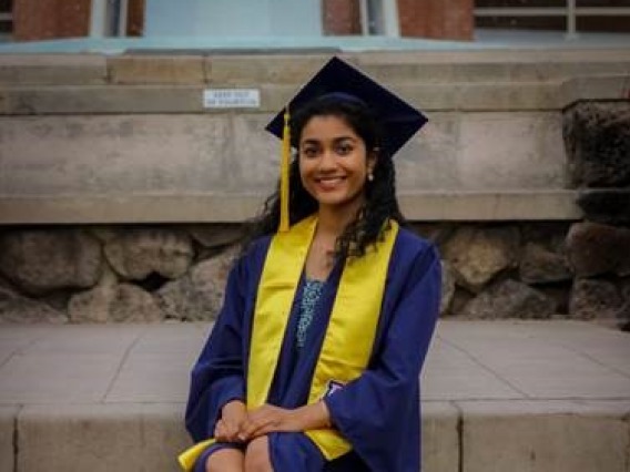 Vara Vungur sitting on steps wearing graduation cap and gown