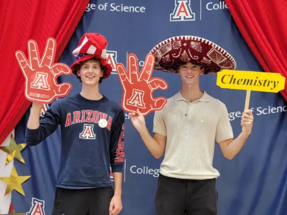 Two students wearing party accessories and the U of A wildcat hand sign