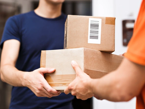 Delivery man in orange shirt, on the right, making two packaged deliveries to a person in a blue shirt on the left.