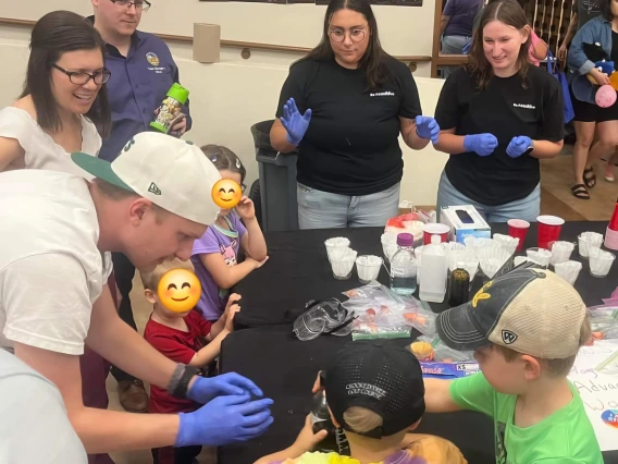 PAWS and young students surrounding a black table doing experiments