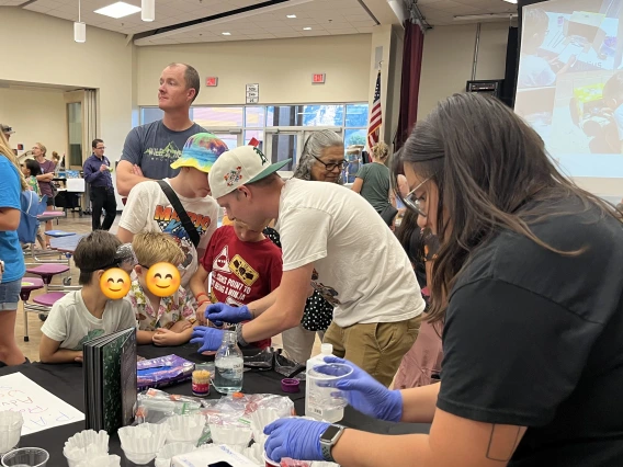 PAWS and young students surrounding a black table doing experiments