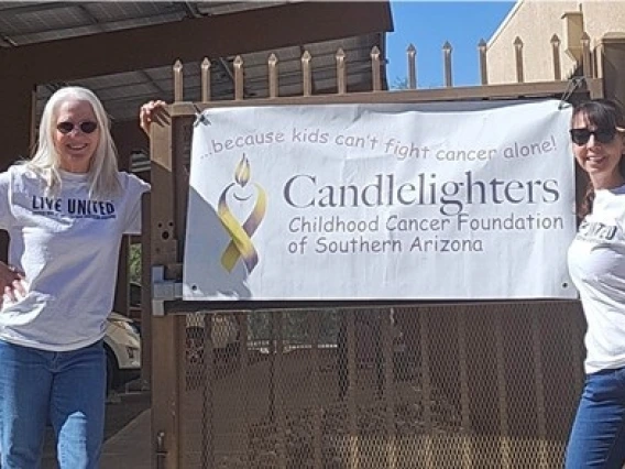 Valerie McClure standing in front of a gate, on the left side with a banner hanging