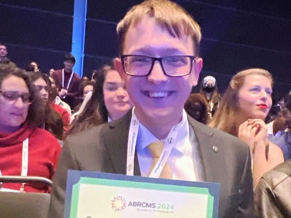 Caleb Konecek holding a certificate for his poster presentation award