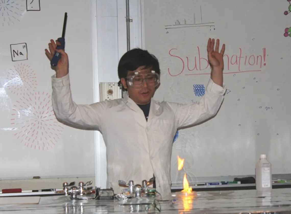 Student in lab coat and goggles performing an experiment with a flame