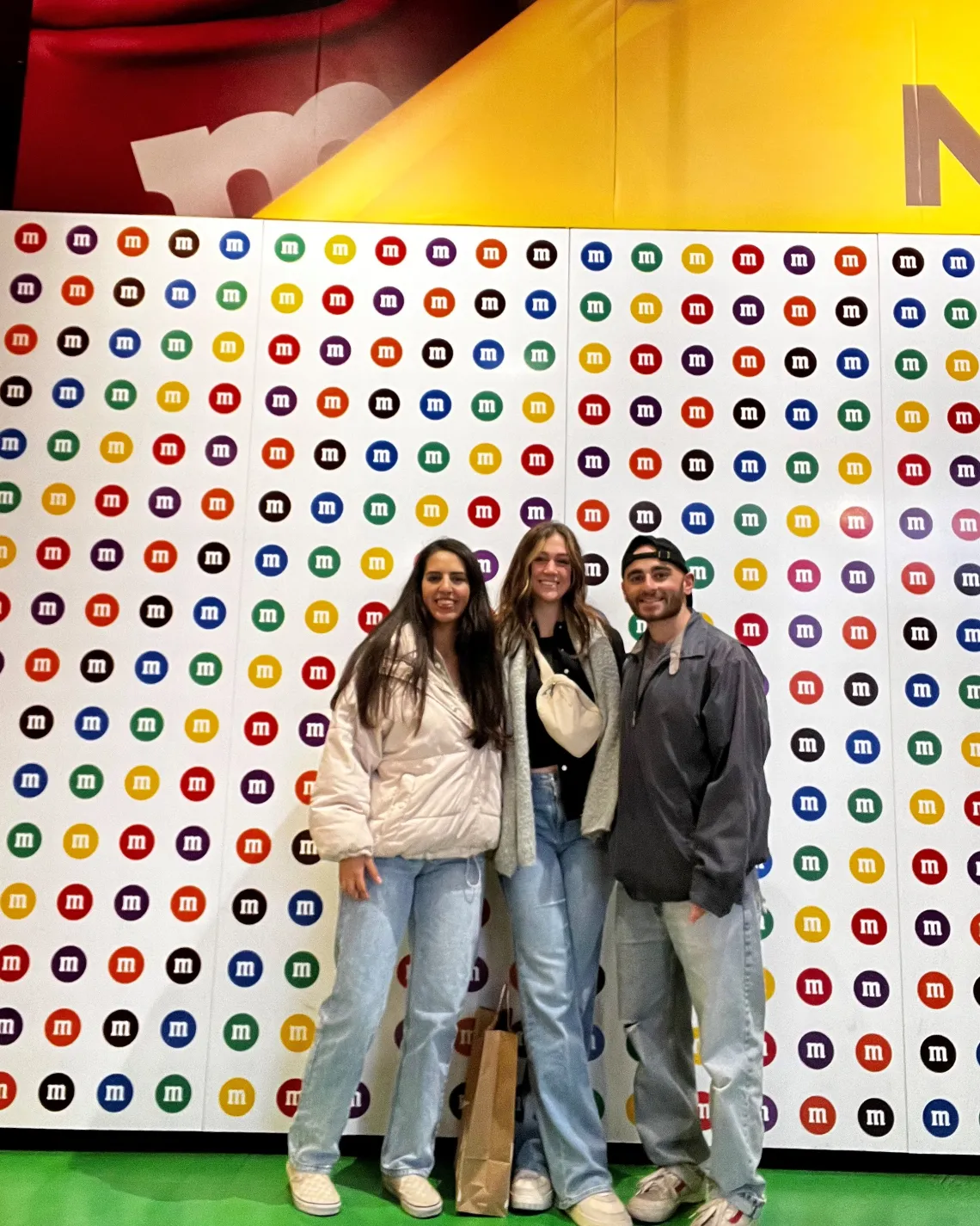 Mayra Rivera, MS, Buchan Lab, Vanessa and Lucas pose in front of M&M themed backboard at the conference