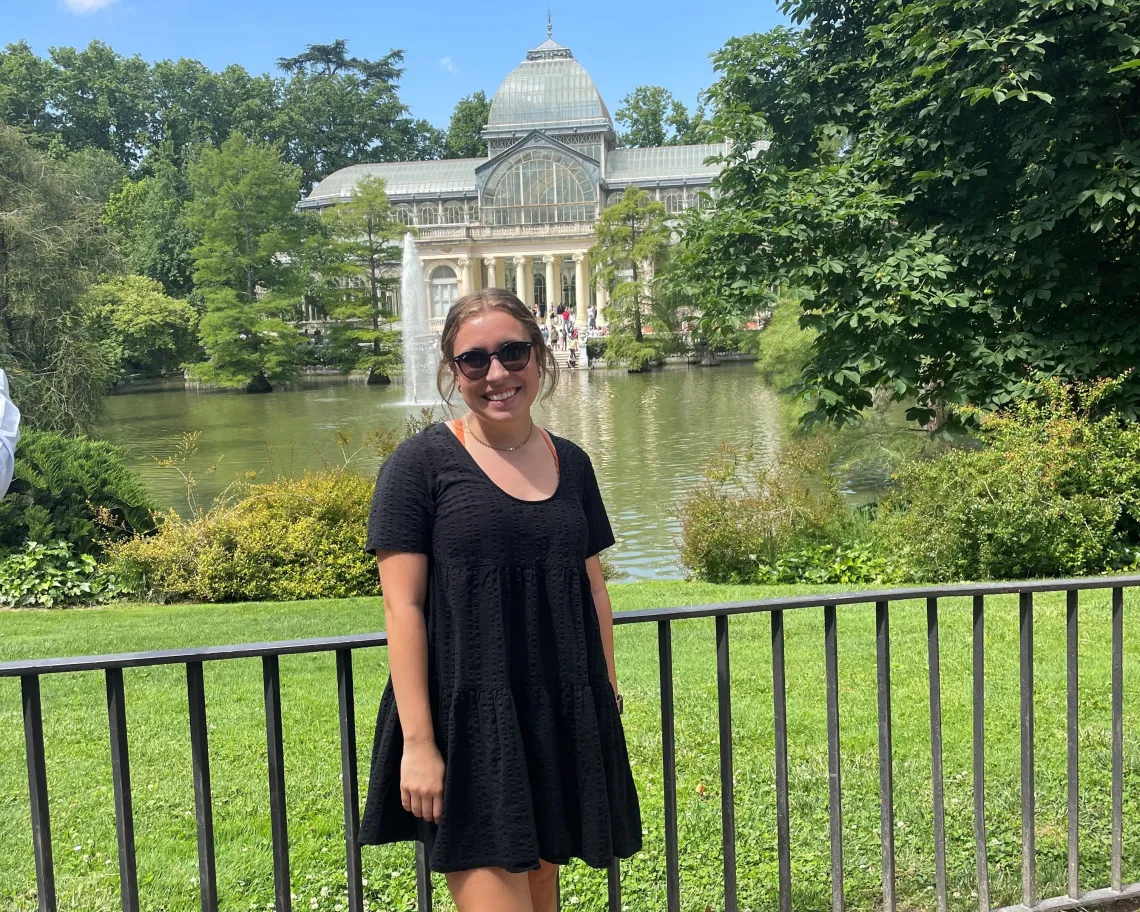 Sarah Sheperd smiling and standing in front of a large white house with a pond and fountain in front of it