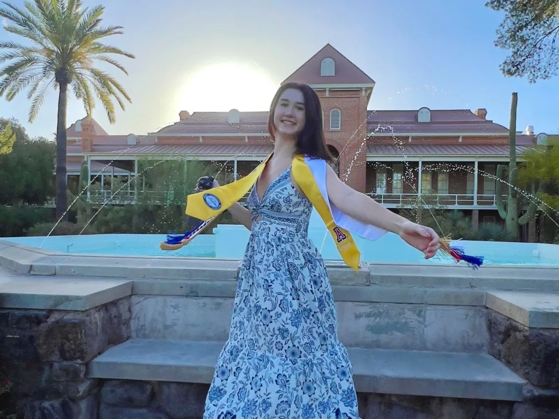 Ellie Browne wearing a blue and white floral dress in front of a fountain.