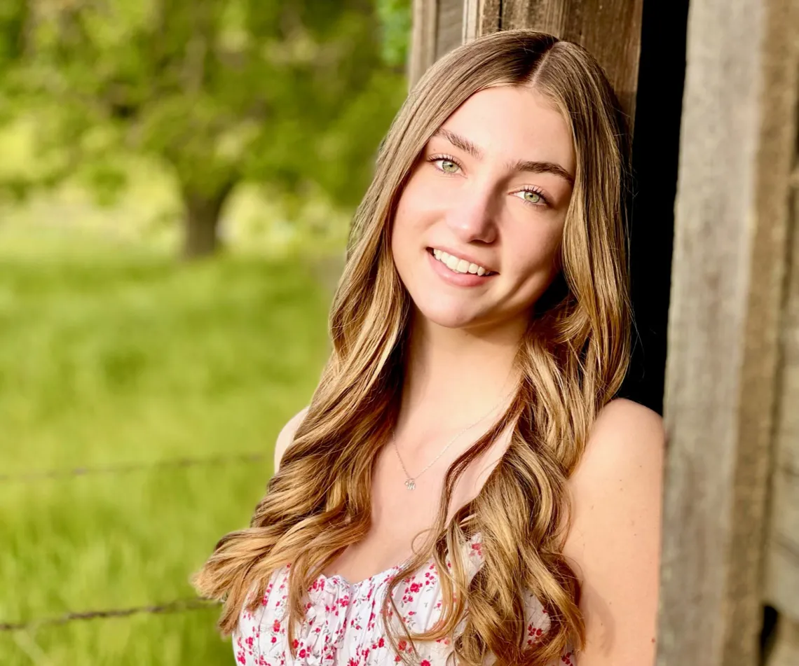 Marley Novak smiling at the camera while outside leaning back against a wooden barn