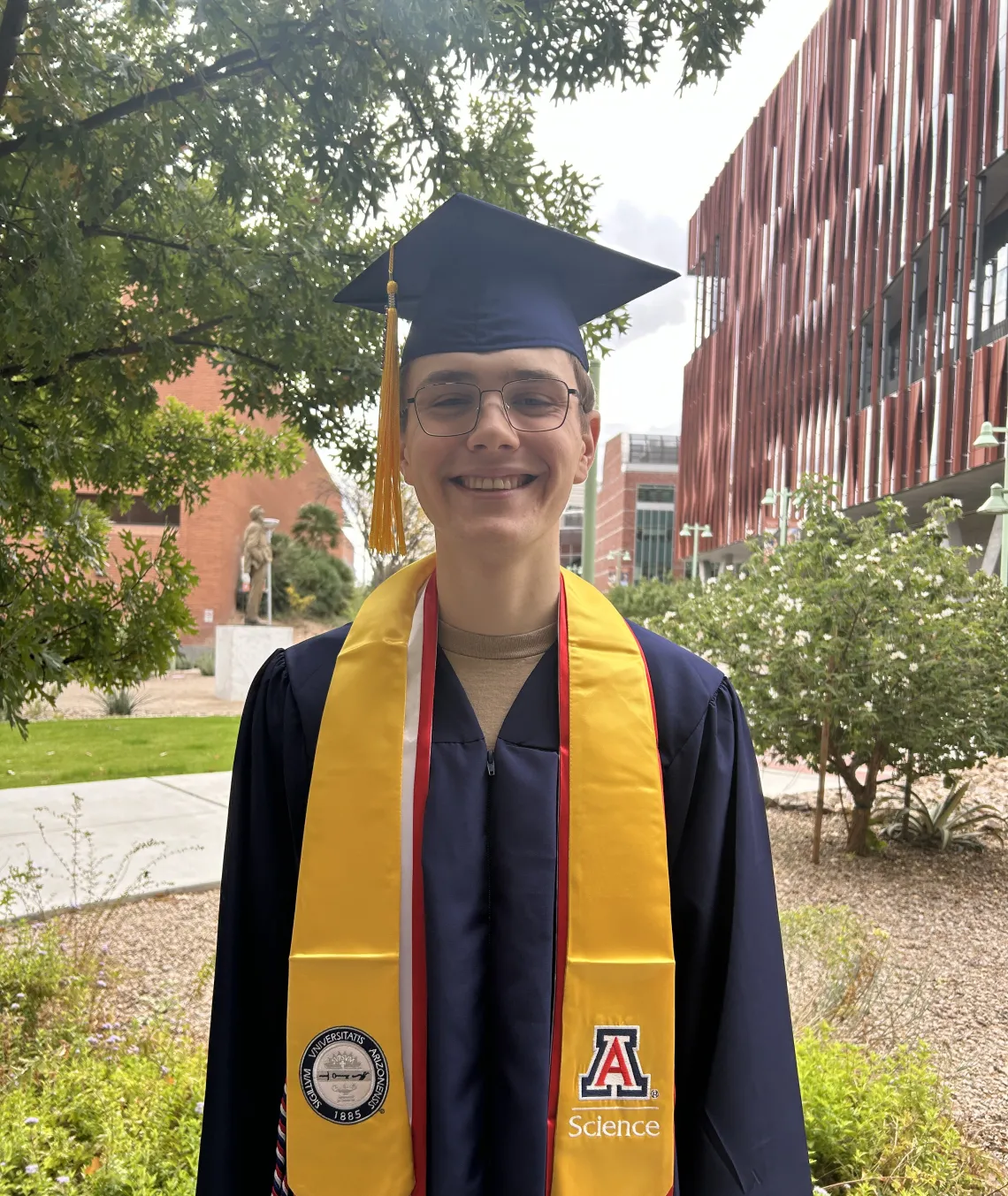 Caleb Seekins stands with large smile in cap and gown