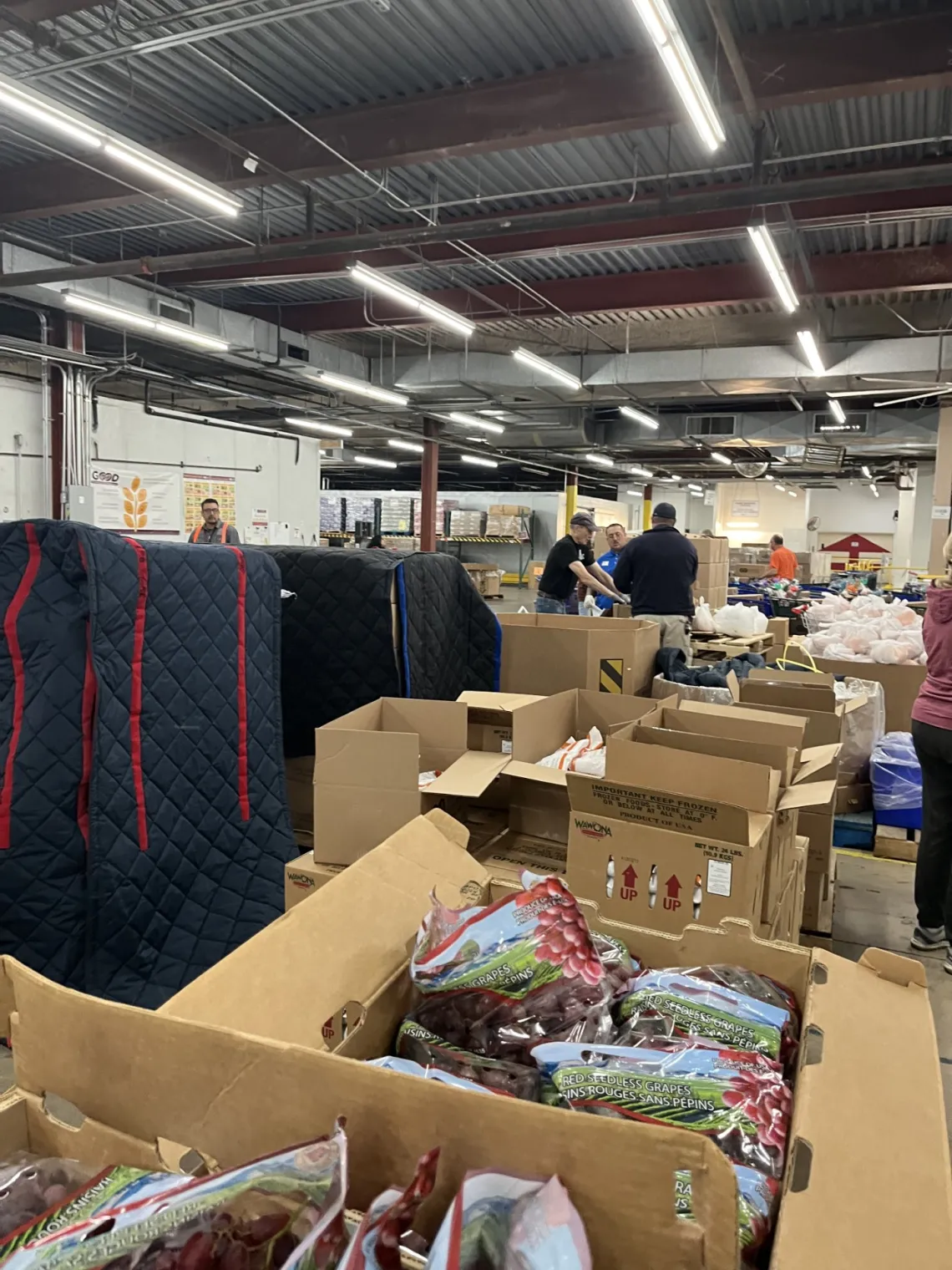 Workers stand in the background with pallets full of items to be distributed to those in need at the Community Food Bank of Southern Arizona