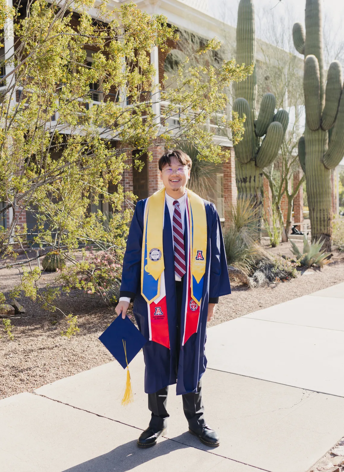 Andrew Leung standing outside Old Main wearing a cap and gown.