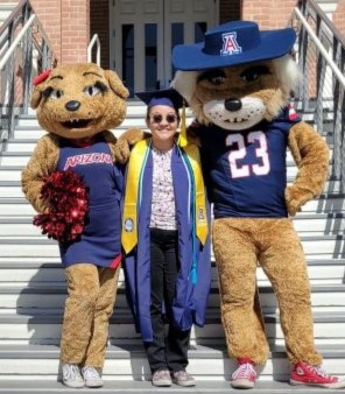 Olivia Bertuca wearing a graduation cap and gown, standing with Wilma and Wilbur Wildcat