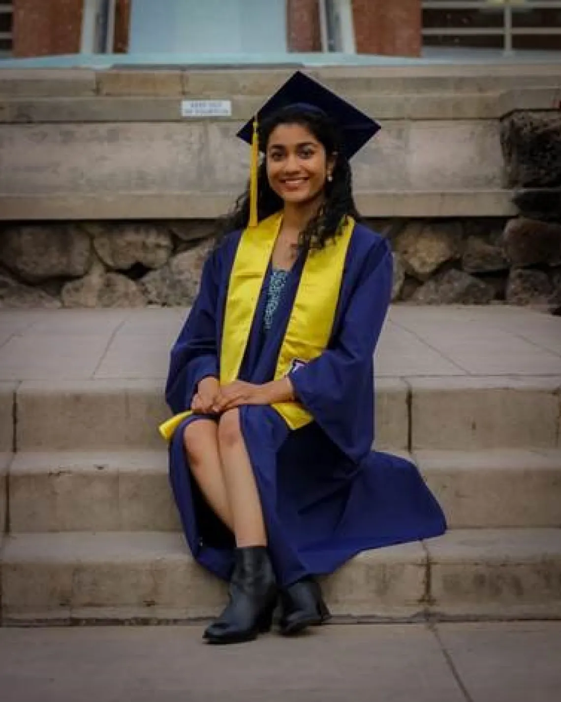 Vara Vungur sitting on steps wearing graduation cap and gown