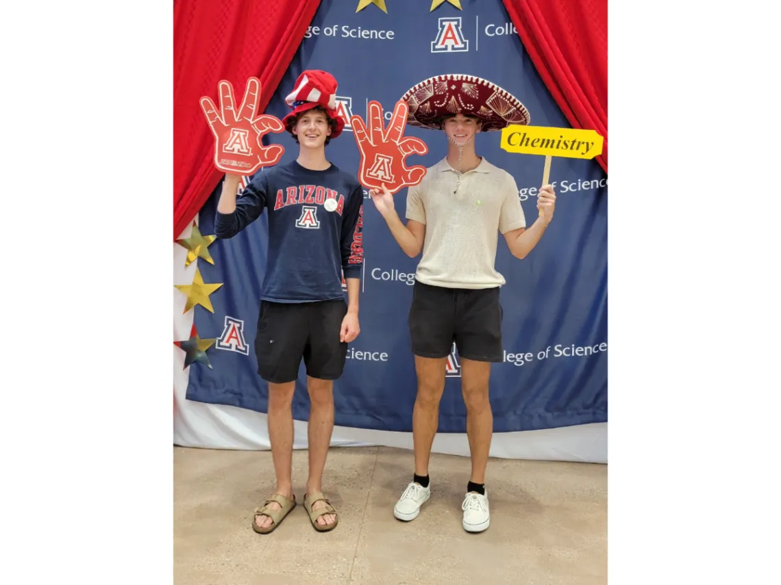 Two students wearing party accessories and the U of A wildcat hand sign