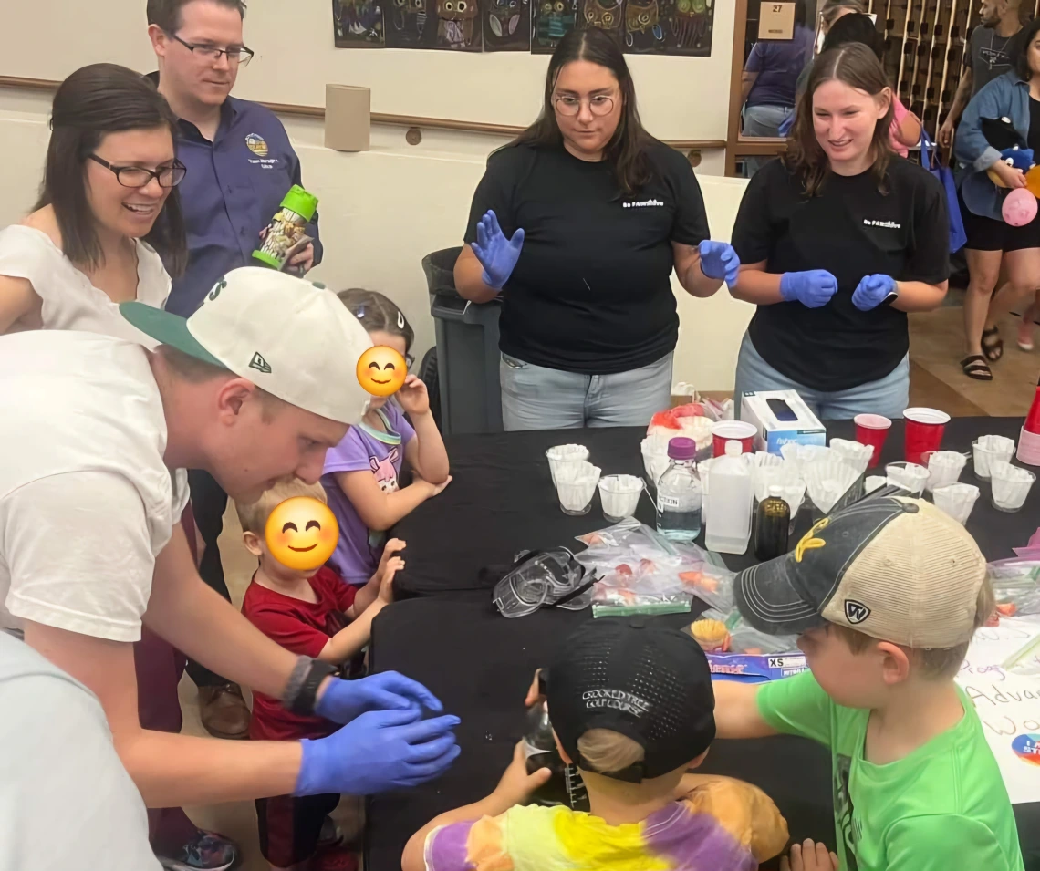 PAWS and young students surrounding a black table doing experiments