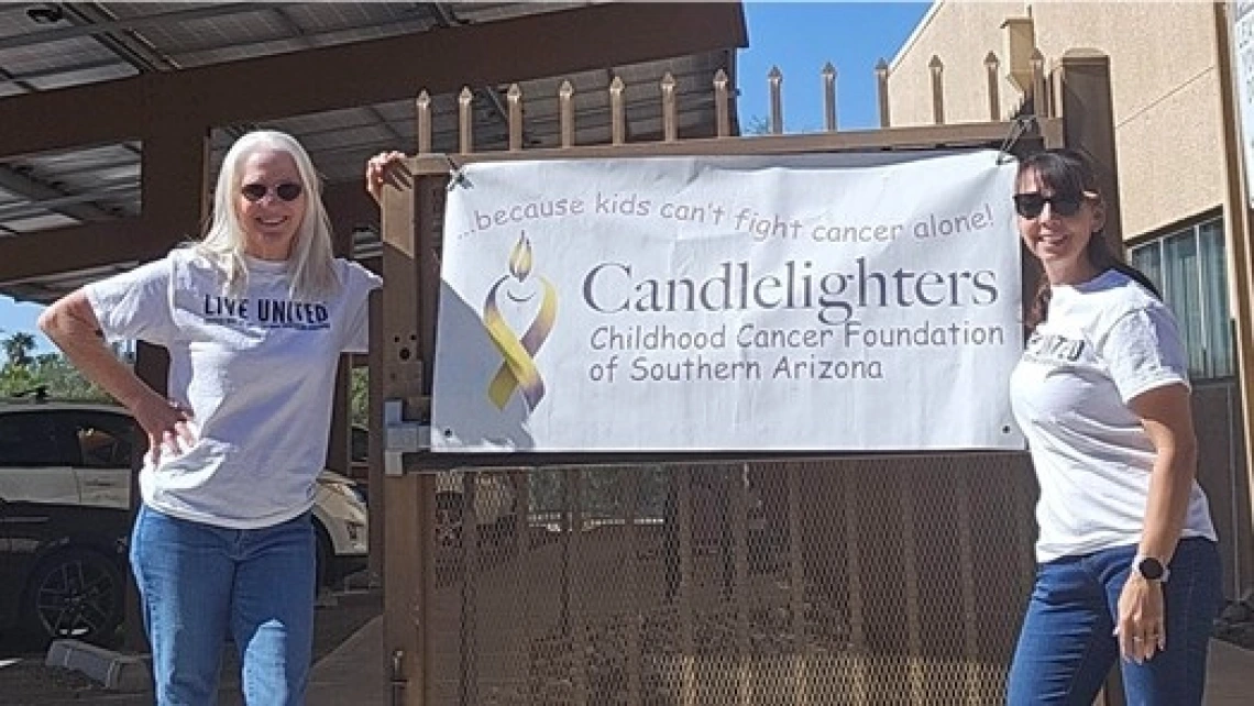 Valerie McClure standing in front of a gate, on the left side with a banner hanging