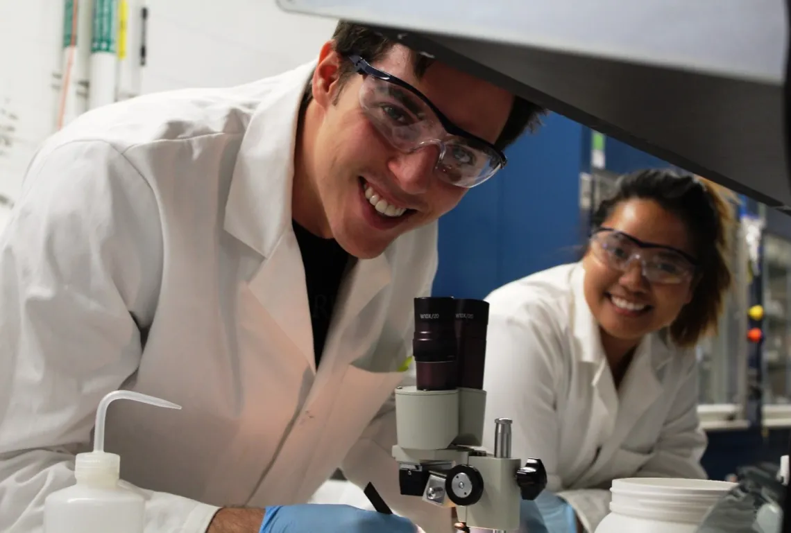 Photo Man and Woman in lab coats and protective glasses working in a UArizona CBC lab