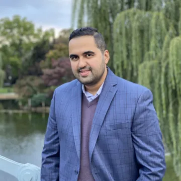 Dr. Alireza Ghanbarpour smiling and standing in front of a pond wearing a suit.