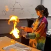 Alyssa Wood in a lab coat conducting an experiment with fire over a lab table